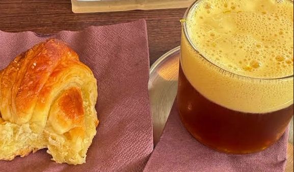 Croissant hojaldrado junto a un café filtrado espumoso