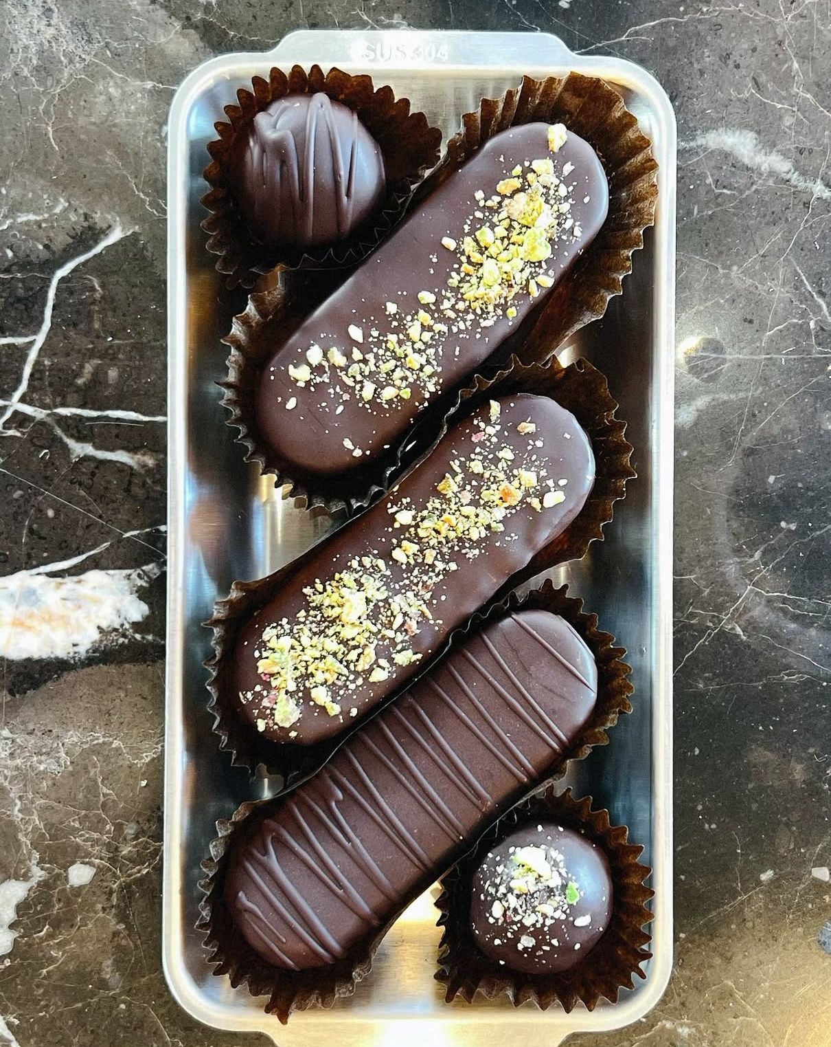 Tres éclairs de chocolate con pistacho en bandeja