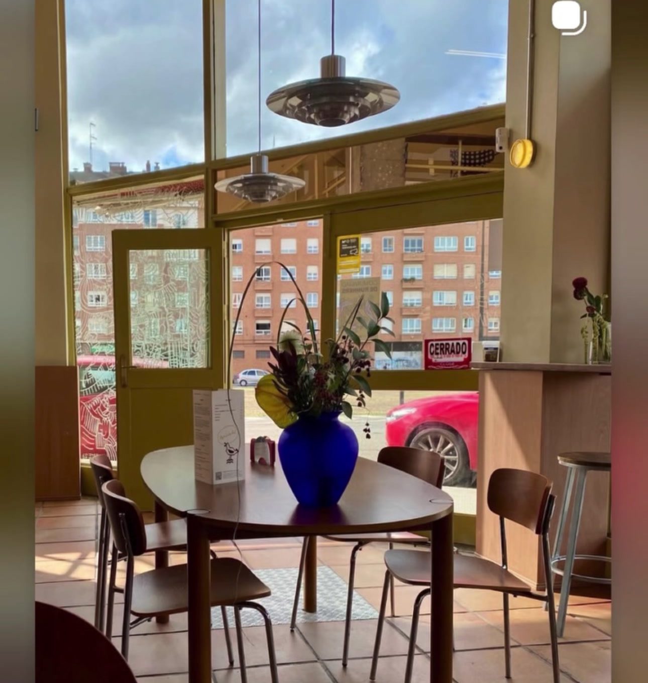 Interior del Under Wonder Cafe: luz de tarde, mesas de madera y un jarrón azul cobalto junto a los ventanales